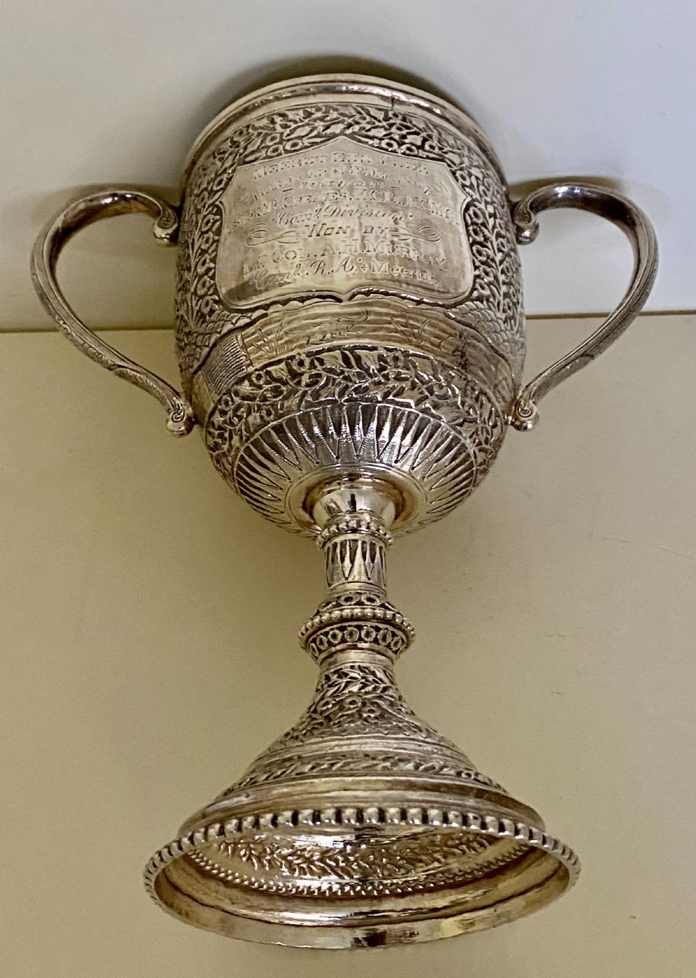 A 19th-century Indian Kutch silver trophy cup featuring dense chased floral motifs, twin scrolled handles, and an engraved central cartouche. View XI