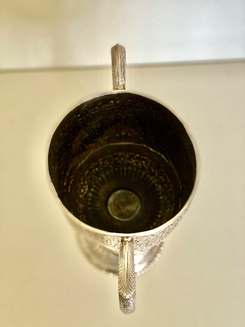 A 19th-century Indian Kutch silver trophy cup featuring dense chased floral motifs, twin scrolled handles, and an engraved central cartouche. View XIV
