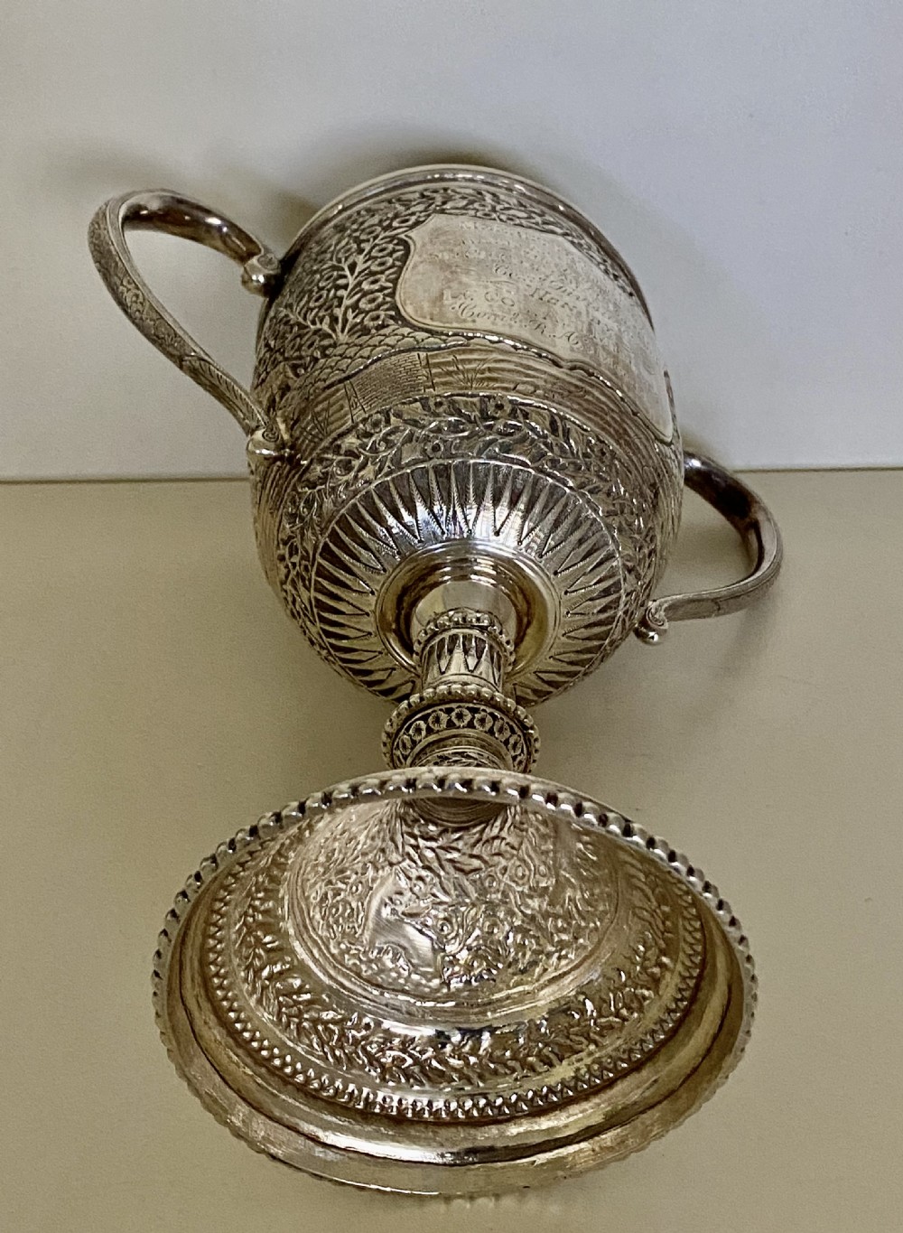 A 19th-century Indian Kutch silver trophy cup featuring dense chased floral motifs, twin scrolled handles, and an engraved central cartouche. View XVI