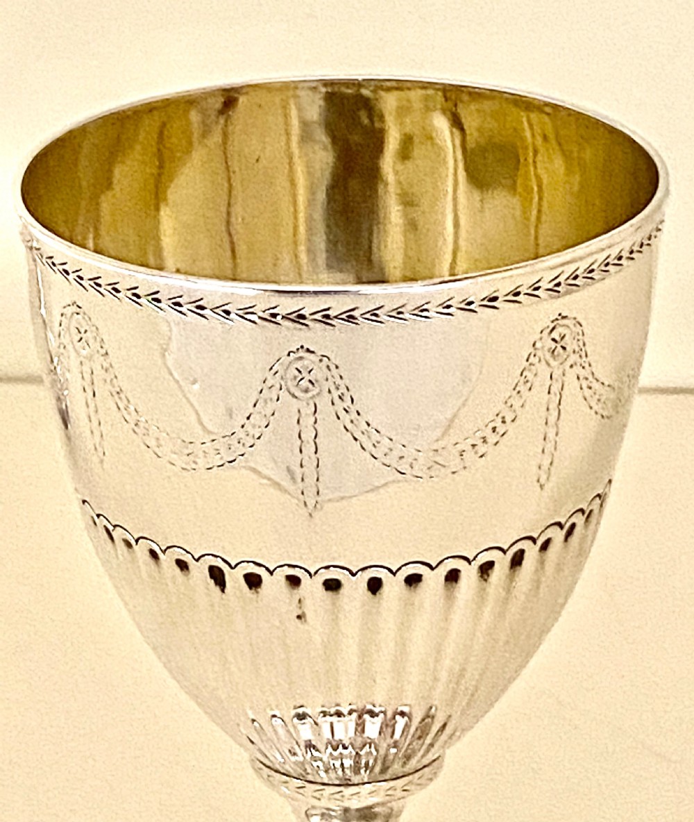 An 18th-century Georgian sterling silver goblet featuring bright-cut festoon engraving, lower bowl fluting, and a circular beaded pedestal foot. View V