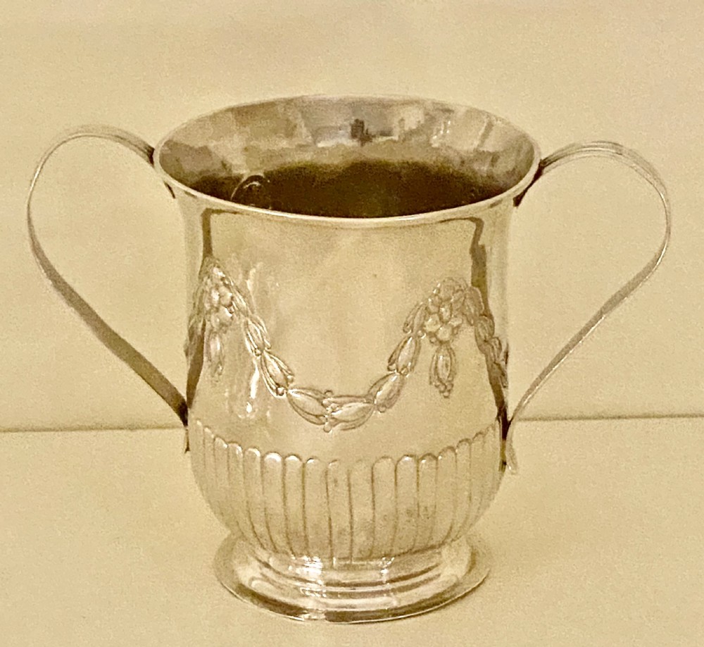 A George III sterling silver two-handled porringer featuring embossed floral swags and vertical fluting around the base. View II