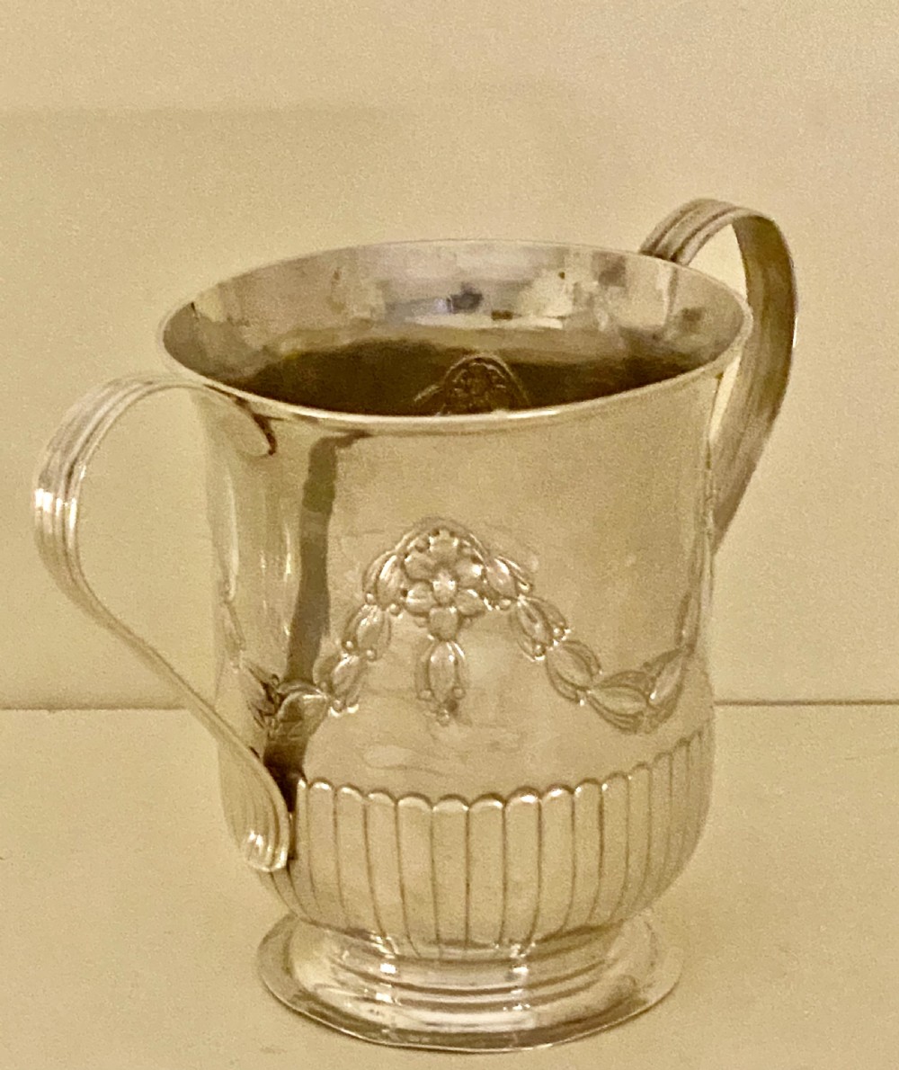A George III sterling silver two-handled porringer featuring embossed floral swags and vertical fluting around the base. View III