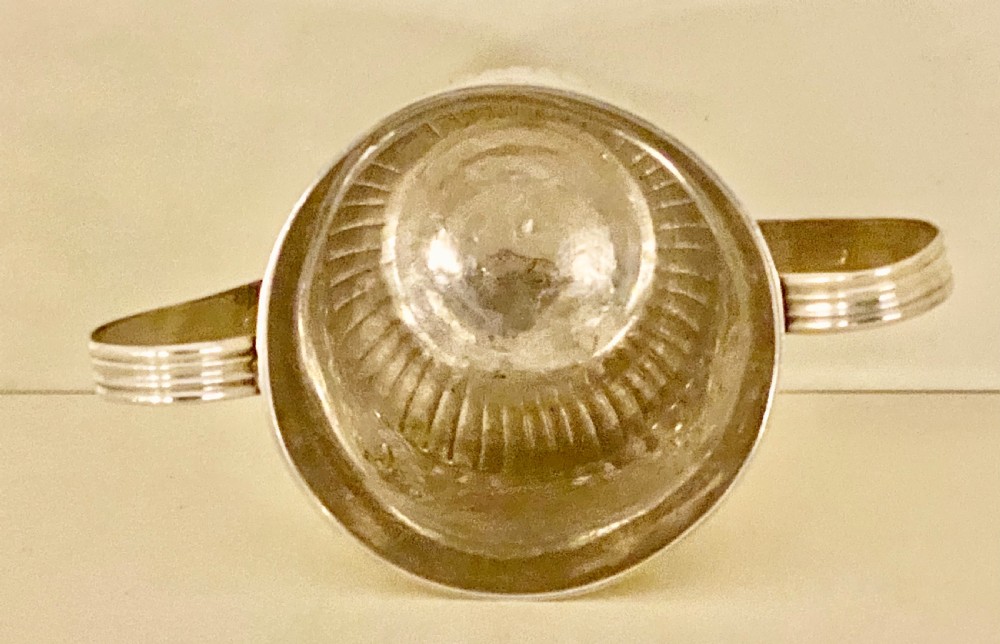 A George III sterling silver two-handled porringer featuring embossed floral swags and vertical fluting around the base. View V