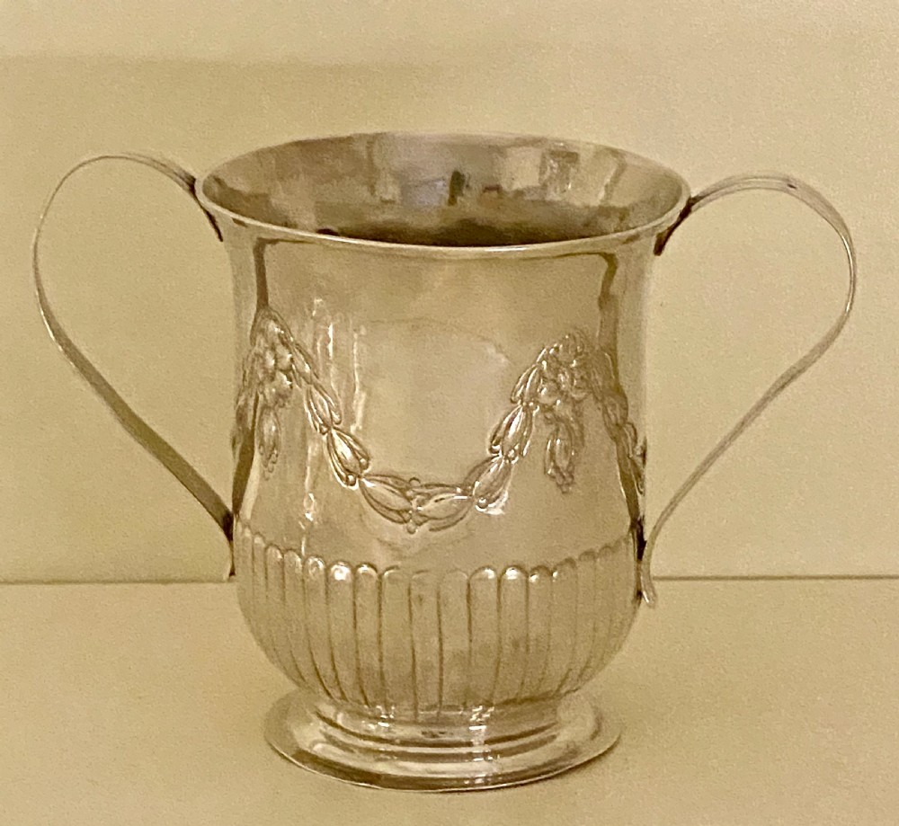 A George III sterling silver two-handled porringer featuring embossed floral swags and vertical fluting around the base. View VII