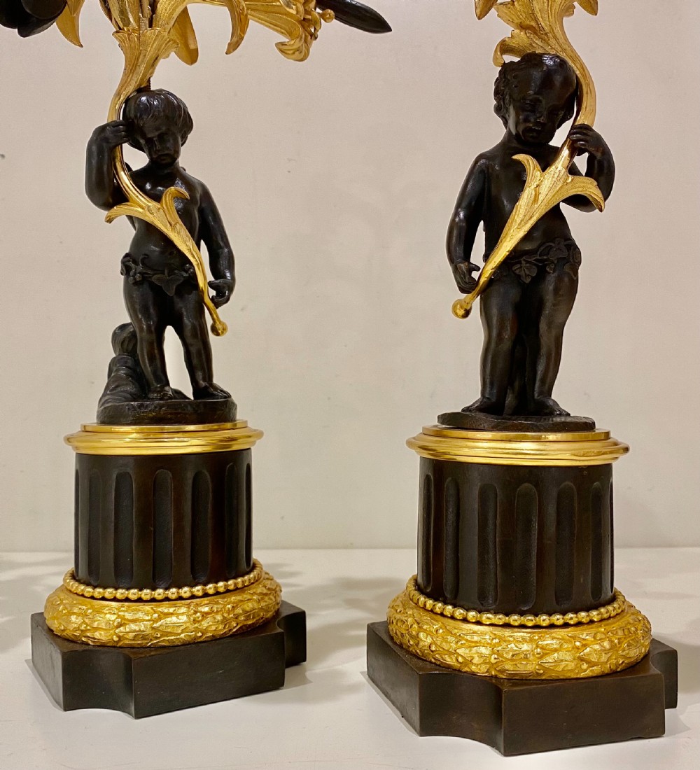 A pair of antique French gilt and patinated bronze candelabra featuring dark bronze cherub figures supporting floral three-light branches on circular bases. View IV