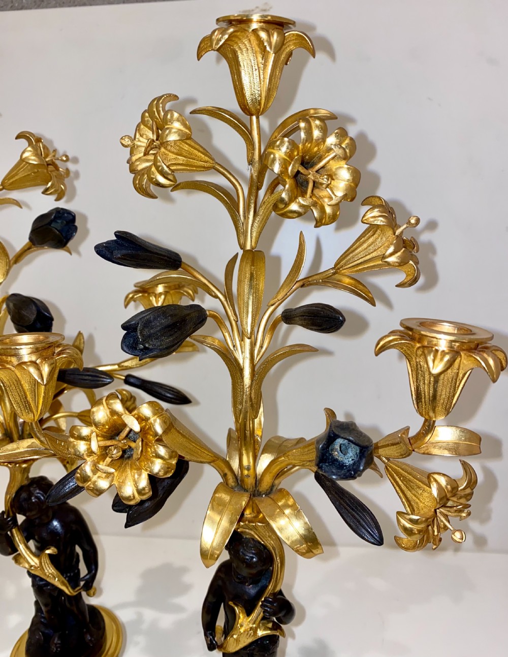 A pair of antique French gilt and patinated bronze candelabra featuring dark bronze cherub figures supporting floral three-light branches on circular bases. View V