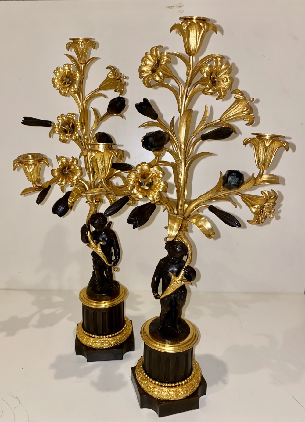 A pair of antique French gilt and patinated bronze candelabra featuring dark bronze cherub figures supporting floral three-light branches on circular bases. View VII