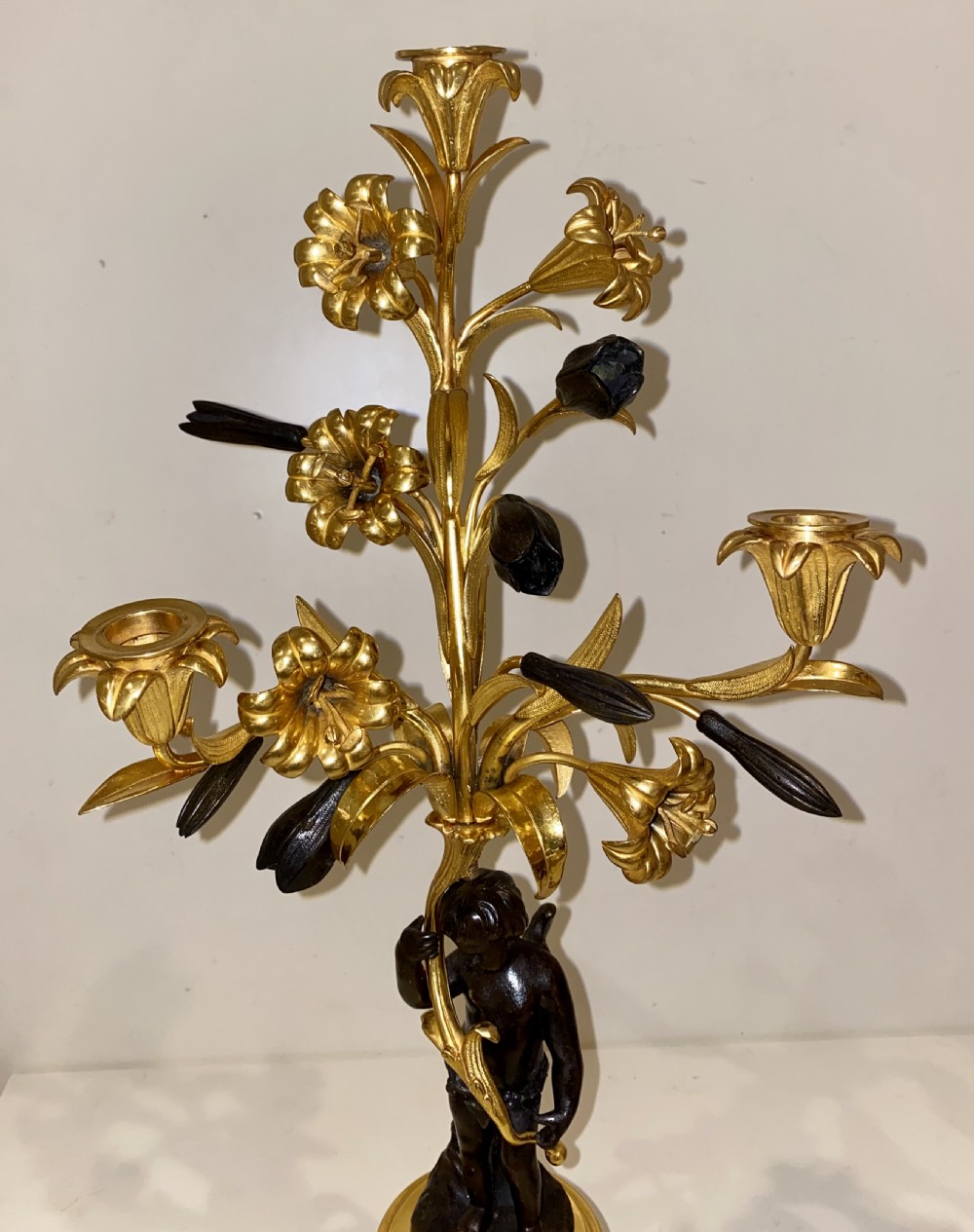 A pair of antique French gilt and patinated bronze candelabra featuring dark bronze cherub figures supporting floral three-light branches on circular bases. View VIII