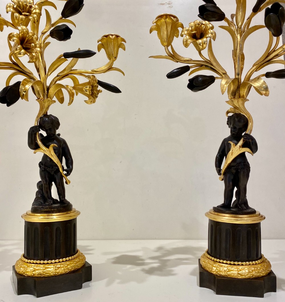 A pair of antique French gilt and patinated bronze candelabra featuring dark bronze cherub figures supporting floral three-light branches on circular bases. View III