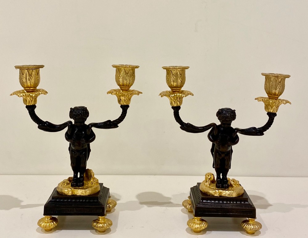 A pair of antique French gilt and patinated bronze two-light candelabra featuring dark bronze cherub figures holding gold candle arms on square bases. View IV