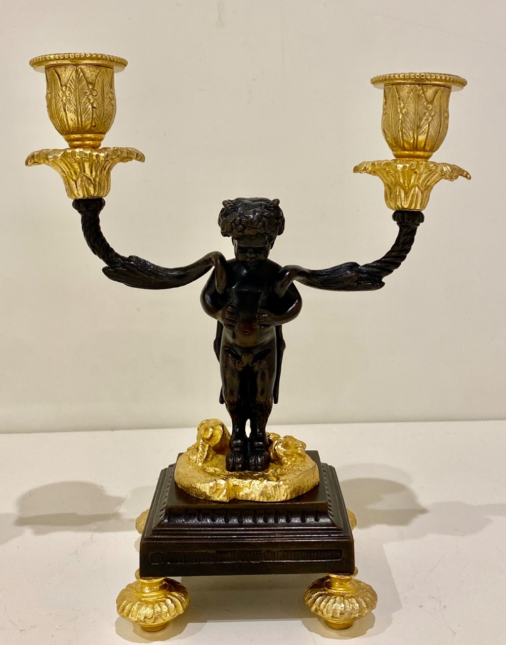 A pair of antique French gilt and patinated bronze two-light candelabra featuring dark bronze cherub figures holding gold candle arms on square bases. View V