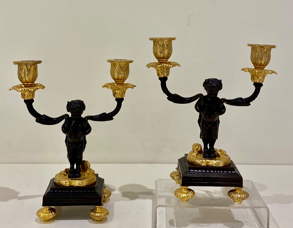 A pair of antique French gilt and patinated bronze two-light candelabra featuring dark bronze cherub figures holding gold candle arms on square bases. View VI