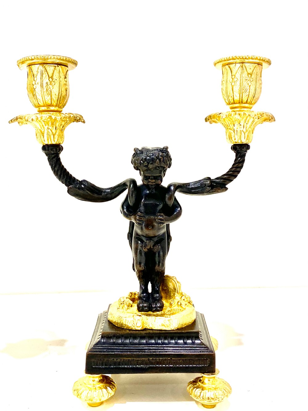 A pair of antique French gilt and patinated bronze two-light candelabra featuring dark bronze cherub figures holding gold candle arms on square bases. View IX
