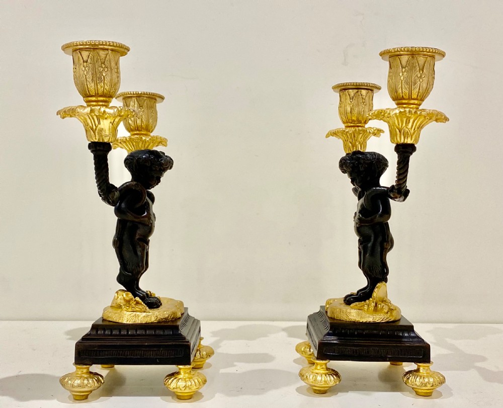 A pair of antique French gilt and patinated bronze two-light candelabra featuring dark bronze cherub figures holding gold candle arms on square bases. View X