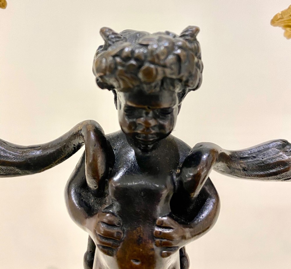 A pair of antique French gilt and patinated bronze two-light candelabra featuring dark bronze cherub figures holding gold candle arms on square bases. View XIV