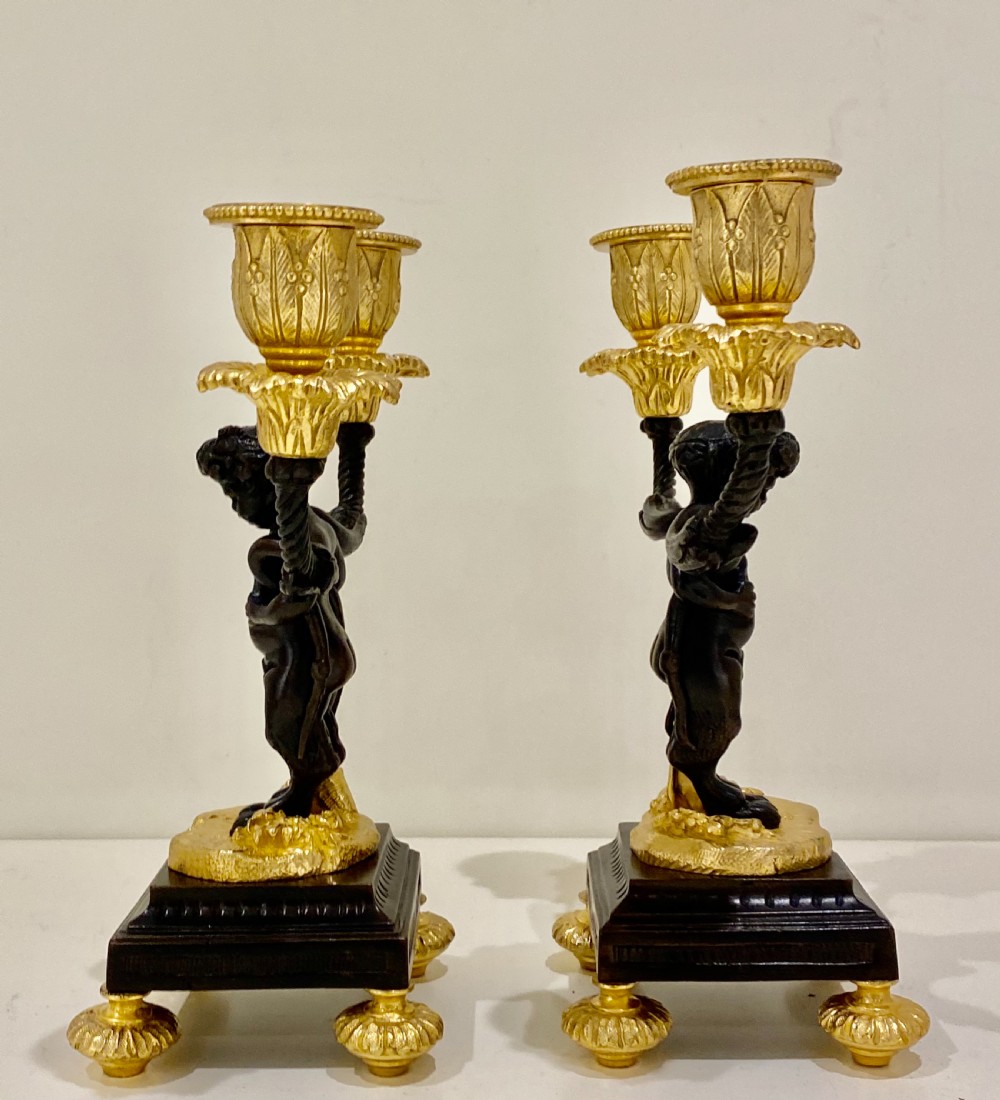 A pair of antique French gilt and patinated bronze two-light candelabra featuring dark bronze cherub figures holding gold candle arms on square bases. View XVI