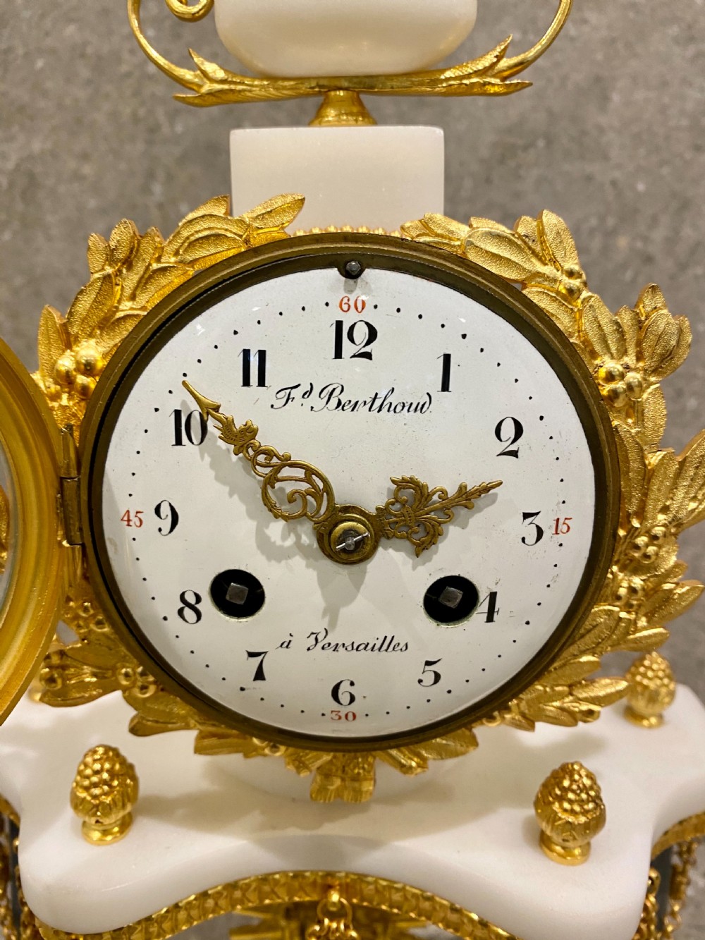 A three-piece Louis XVI style clock garniture set featuring a central white and grey marble clock adorned with gilt bronze mounts and a sunburst pendulum, flanked by two matching marble obelisk candle holders. View V