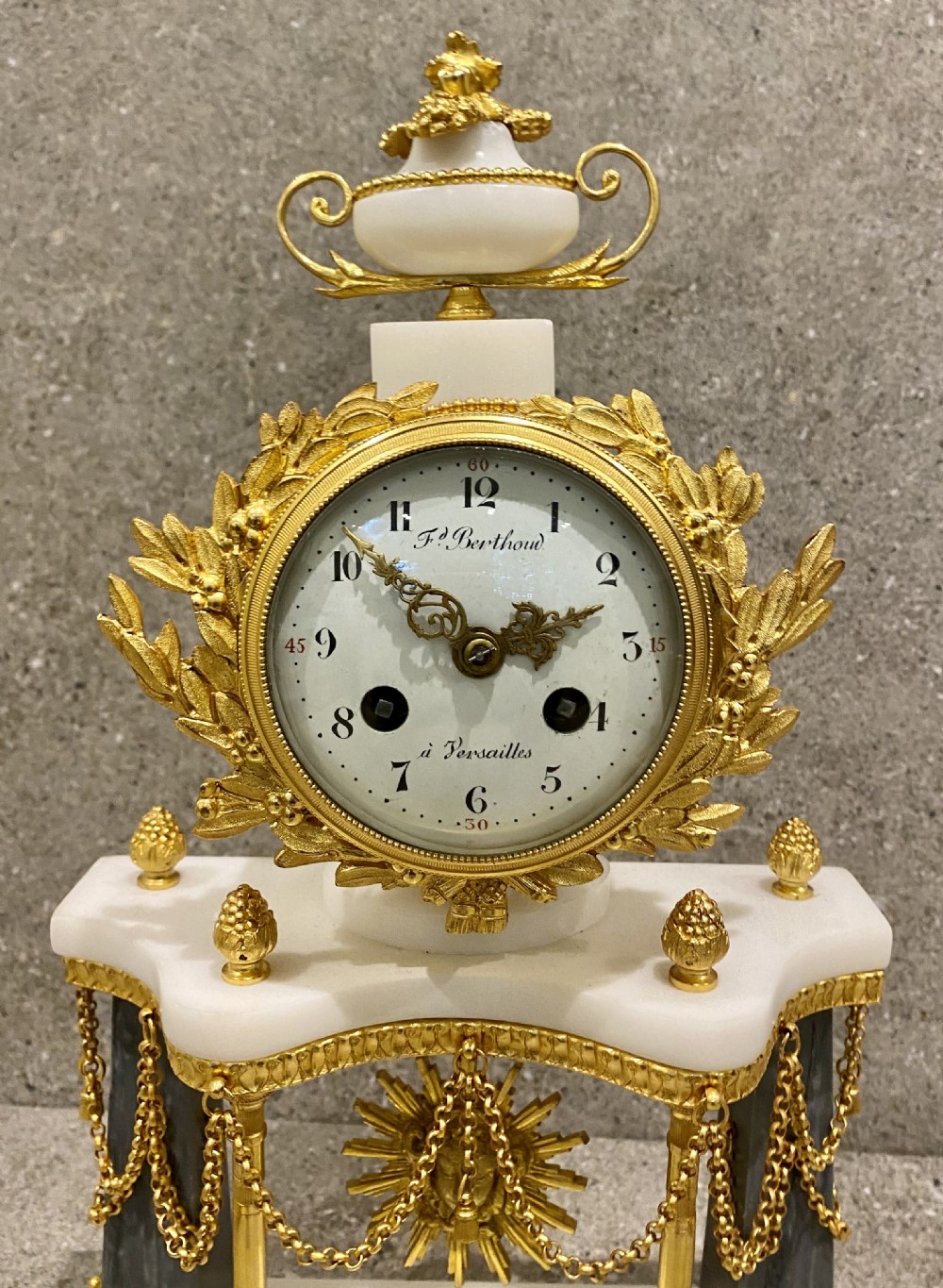 A three-piece Louis XVI style clock garniture set featuring a central white and grey marble clock adorned with gilt bronze mounts and a sunburst pendulum, flanked by two matching marble obelisk candle holders. View VI