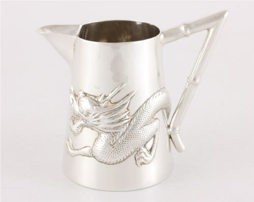 fig 1. A silver jug with a repousse dragon around the body and a handle shaped like bamboo.