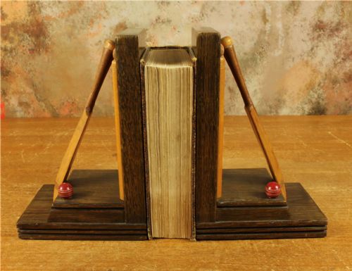 fig 1. A pair of carved dark oak bookends featuring miniature wooden cricket bats, wickets, and red painted cricket balls mounted on stepped rectangular bases.