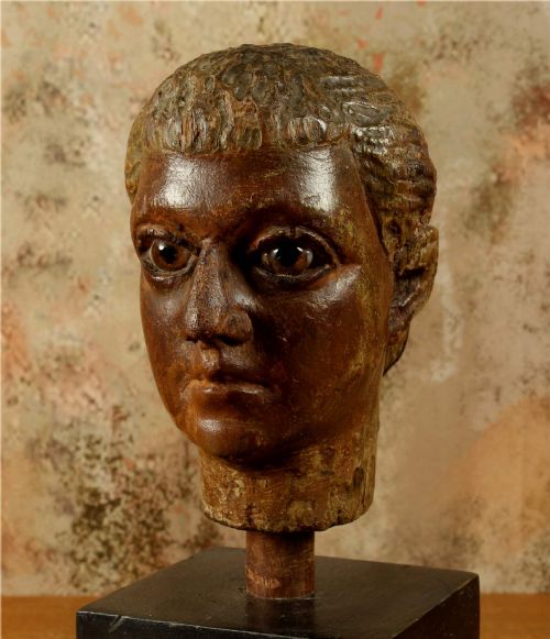 fig 1. An 18th-century Italian carved wooden head with remnants of polychrome finish, mounted on a dark cubic wooden display plinth.