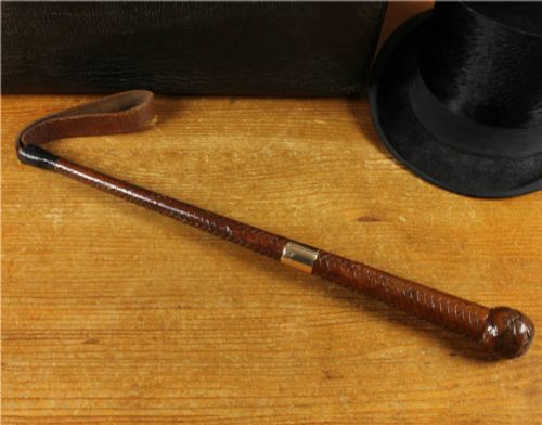 fig 1. An antique woven dark brown leather riding crop featuring a polished gold collar band and a leather keeper loop at the tip.