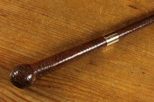 fig 3. An antique woven dark brown leather riding crop featuring a polished gold collar band and a leather keeper loop at the tip.