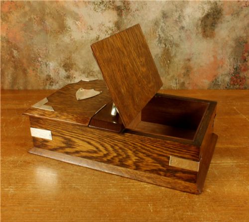 fig 2. A rectangular dark oak wooden box featuring dual hinged lids, a central metal handle, silver corner mounts, and silver shield motifs on each lid.