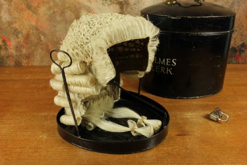 fig 2. An antique legal set comprising a woven horsehair barrister wig on a metal stand beside a cylindrical black tin carrying case with cream lettering reading Eric C. Holmes Town Clerk.