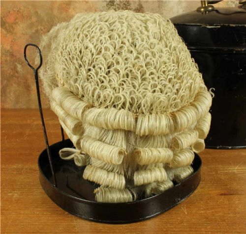 fig 3. An antique legal set comprising a woven horsehair barrister wig on a metal stand beside a cylindrical black tin carrying case with cream lettering reading Eric C. Holmes Town Clerk.