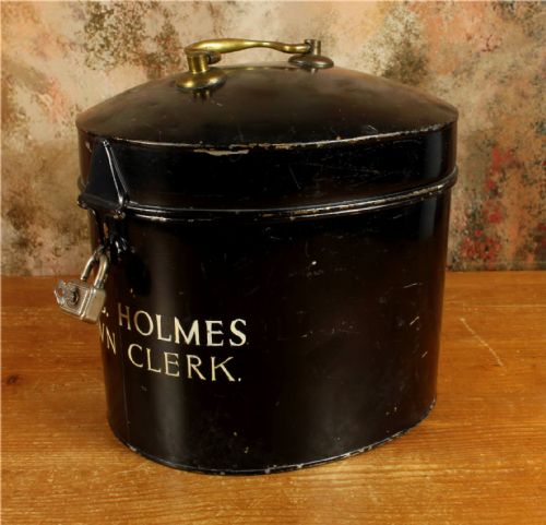 fig 4. An antique legal set comprising a woven horsehair barrister wig on a metal stand beside a cylindrical black tin carrying case with cream lettering reading Eric C. Holmes Town Clerk.