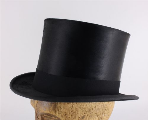 fig 2. A black silk plush top hat with a grosgrain ribbon band resting on top of an oval hat box.