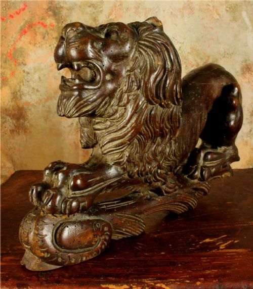 fig 1. A carved dark wood lion sculpture shown in a reclining position with an open mouth and detailed mane.