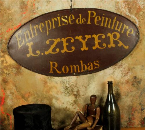 fig 1. An oval dark brown metal trade sign featuring hand-painted yellow French lettering.