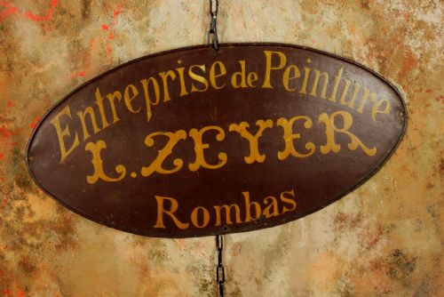 fig 2. An oval dark brown metal trade sign featuring hand-painted yellow French lettering.
