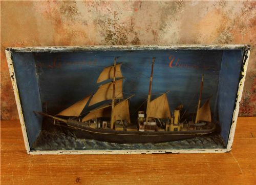fig 1. A handcrafted 19th-century ship diorama set inside a blue painted wooden box featuring a vessel with sails and steam funnel set upon sculpted waves.