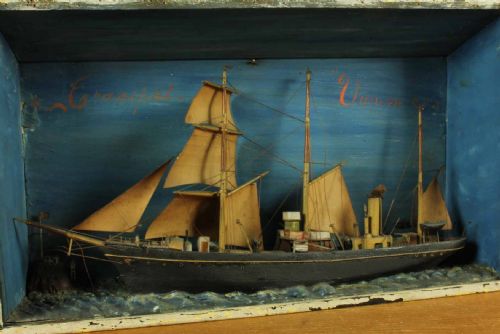 fig 2. A handcrafted 19th-century ship diorama set inside a blue painted wooden box featuring a vessel with sails and steam funnel set upon sculpted waves.