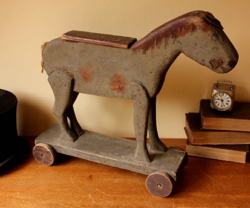 fig 1. A carved wooden pull toy depicting a horse or donkey with distressed grey paint, mounted on a base with four small wooden wheels.