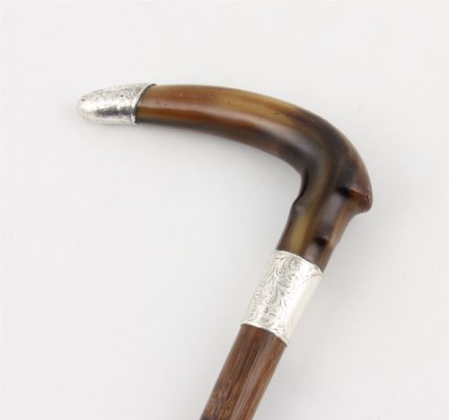 fig 2. An Edwardian walking stick featuring a curved brown horn handle with a silver tip and an engraved sterling silver collar attached to a dark bamboo shaft.