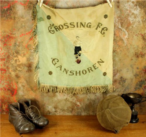 fig 1. A square two-tone silk banner featuring pale green and cream diagonal panels, embroidered lettering reading Crossing FC Ganshoren, a central footballer figure, and fringe trim.
