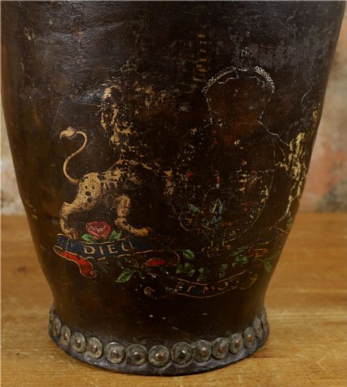 fig 2. A dark brown Georgian leather fire bucket featuring a heavy strap handle, brass studs around the base, and a painted royal coat of arms with a lion and unicorn.