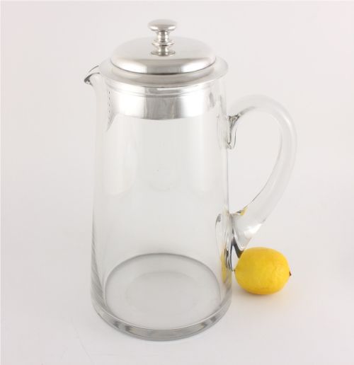 fig 1. A clear glass water jug with a silver-plated hinged lid, integrated strainer spout, and curved glass handle.