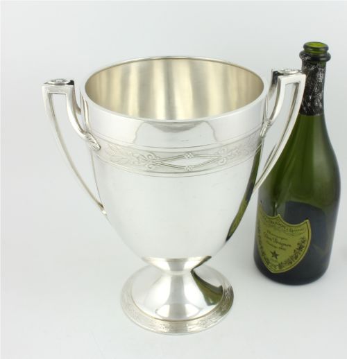 fig 1. An antique silver-plated urn-shaped champagne cooler featuring twin angular handles, a foliage engraved band, and a stepped pedestal foot.