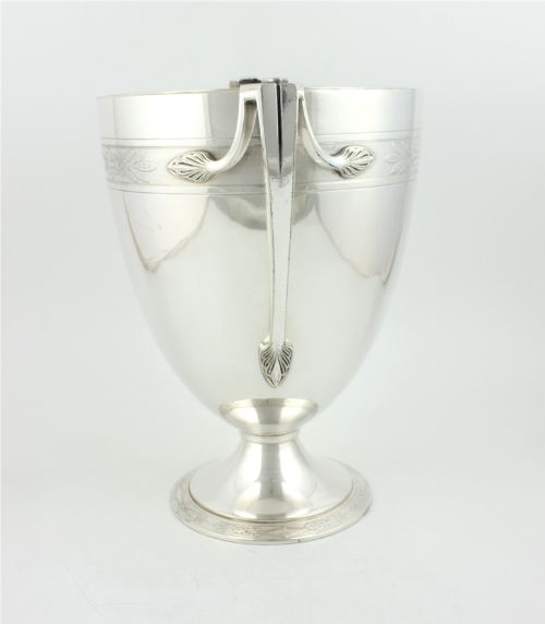 fig 2. An antique silver-plated urn-shaped champagne cooler featuring twin angular handles, a foliage engraved band, and a stepped pedestal foot.