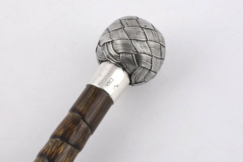 fig 2. A close-up of an antique walking stick featuring a woven silver wire knot handle mounted on a dark bamboo shaft with a silver collar.
