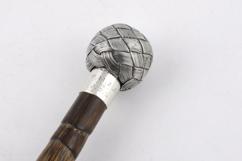 fig 3. A close-up of an antique walking stick featuring a woven silver wire knot handle mounted on a dark bamboo shaft with a silver collar.