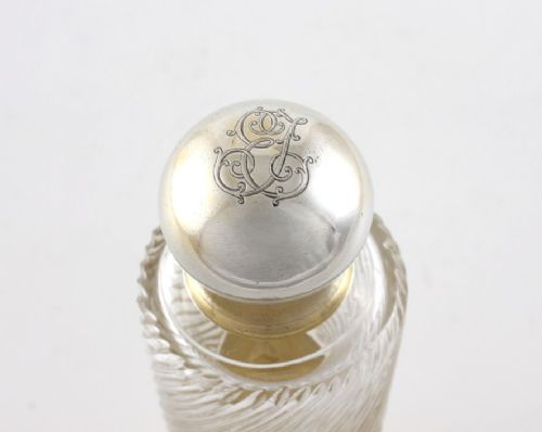A cylindrical clear glass flask featuring spiral fluting, topped with a domed silver cap and a silver base bearing an engraved monogram. View V