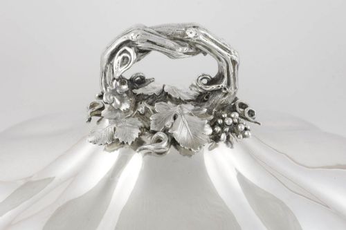 fig 1. A Georgian Old Sheffield plate silver meat dome featuring a fluted body, an engraved heraldic coat of arms, and a cast handle adorned with vine leaves and grapes.