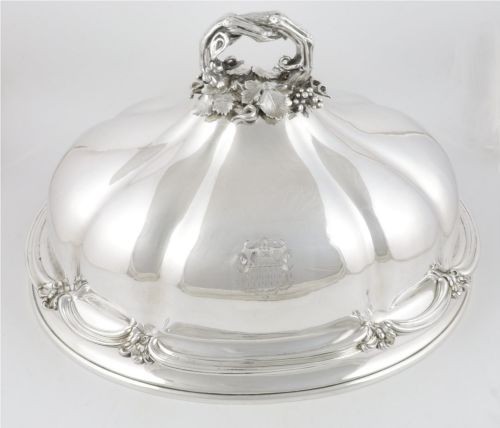 fig 2. A Georgian Old Sheffield plate silver meat dome featuring a fluted body, an engraved heraldic coat of arms, and a cast handle adorned with vine leaves and grapes.