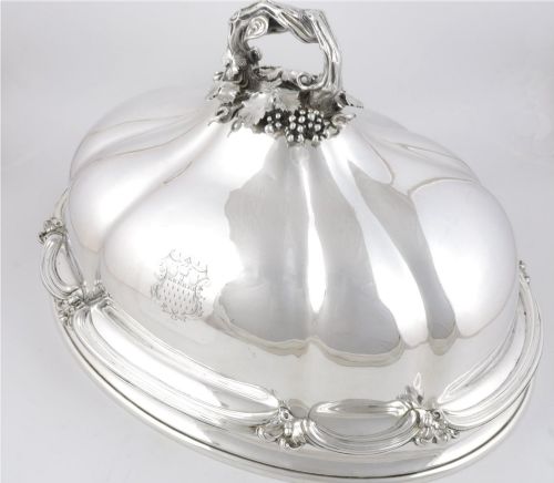fig 3. A Georgian Old Sheffield plate silver meat dome featuring a fluted body, an engraved heraldic coat of arms, and a cast handle adorned with vine leaves and grapes.